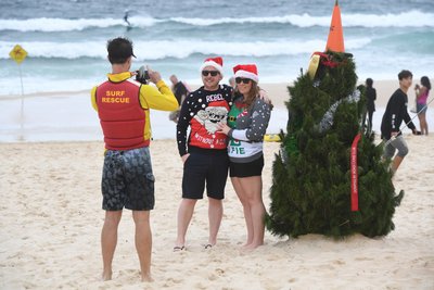 Ein Pärchen am australischen Strand Bondi Beach lässt sich von einem Rettungsschwimmer neben einem Weihnachtsbaum fotografieren.