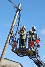 Feuerwehrleute kappen die Leitung, damit der Telefonmast nicht auf die Straße stürzt. 