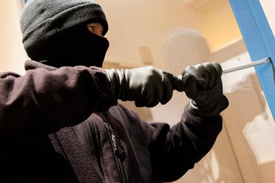 Symbolbild: Ein als Einbrecher verkleideter Mann hebelt ein Fenster auf.