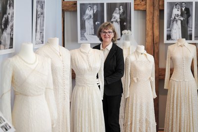 Kuratorin Katrin Färber mit zwei Brautkleidern an ihren Seiten, die jeweils am 8. Oktober 1949 zur Hochzeit getragen wurden.