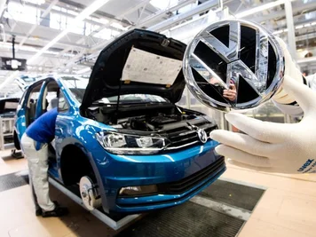 Ein Mitarbeiter zeigt ein VW Logo kurz vor Einbau in einen Volkswagen Touran.