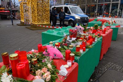 Blumen, Kuscheltiere und Kerzen stehen auf farbigen Betonpollern, die zum Schutz des Magdeburger Weihnachtsmarktes aufgestellt wurden. 