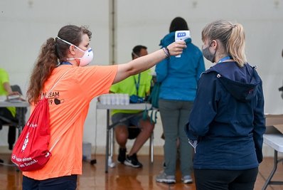 Eine Helferin misst Fieber bei einer Probandin, die an einem Großversuch der Universitätsmedizin Halle/Saale in der Arena Leipzig teilnimmt.