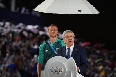 Diesen Volunteer haben Millionen Fernsehzuschauer in Großaufnahme gesehen: Der junge Mann hielt IOC-Präsident Thomas Bach während seiner Eröffnungsrede im strömenden Regen den Schirm.