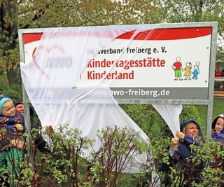 Gemeinsam mit ihren Erzieherinnen Petra Morgenstern (r.) und Sylvia Donat enthüllen die Kinder Roxy (r.) und Jonas die neue Namenstafel ihrer Kindertagesstätte. 