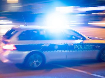             Ein Polizeiauto fährt unter Einsatz von Blaulicht und Sirene eine Straße entlang.