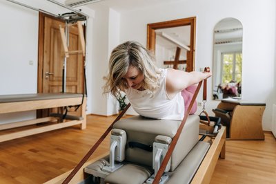 Beim Reformer-Pilates werden Übungen auf einem speziellen Gerät mit beweglicher Liegefläche, Federn und Seilzügen ausgeführt.