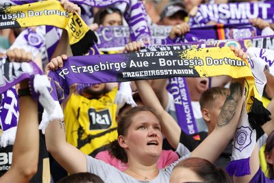 Fans von Erzgebirge Aue halten extra für das Spiel gegen Dortmund hergestellte Schals in die Luft.