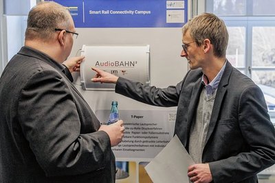 Onno Szillis (l.) von der Deutschen Bahn lässt sich von TU-Mitarbeiter Georg Schmidt einen Lautsprecher aus recycelbarem Papier- und Folienmaterial erklären.  