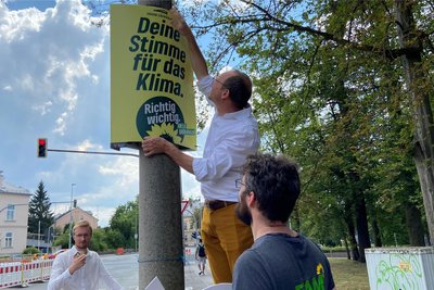 Wolfram Günther hängt in Freiberg ein Plakat auf. An dem heißen Sonntagnachmittag sind kaum Menschen in der Freiberger Innenstadt unterwegs.