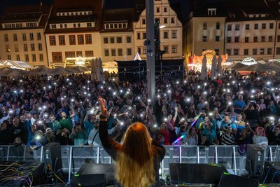 Bergstadtfest 2025: Tausende Menschen schwenken Taschenlampen bei einem Konzert auf dem Freiberger Obermarkt.
