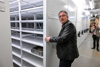 Museumschef Ronny Rößler zeigt die noch weitgehend leeren Regale. Diese stehen auf Gleisen und können mit den Kurbeln an der Seite hin- und her bewegt werden.