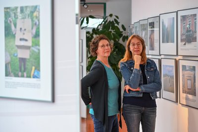 Susanne Krujatz und rechts Anja Merkel in der Ausstellung „Endlich Leben“. Sie zeigt auch Positives wie ein Kind, das sich mit einem Karton verkleidet hat.