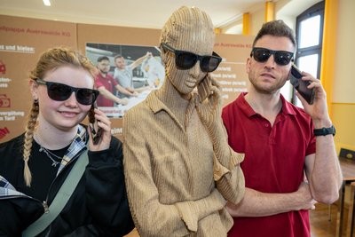 Leonie am Stand der Wellpappe Auerswalde KG mit einer Figur aus Wellpappe und Abteilungsleiter Pierre Richter.