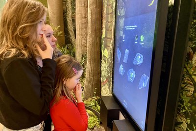 Charlott Bretschneider rätselt mit der großen Schwester Clara und Mama Claudia an einem der Interaktionsterminals, die zum Spiel um das leuchtende Kohlestück zählen.