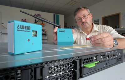 PTS-Geschäftsführer Lutz Scheibe zeigt die Erfindung aus Ottendorf: Der Sensor bzw. das Messgerät (links oben) signalisieren, wenn ein Computer (unten) beispielsweise zu heiß wird. Das Signal trifft auf den Empfänger (rechts oben), der wiederum per SMS aufs Handy die Information weitergibt.