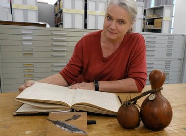 Museumsleiterin Sina Lorbeer-Klausnitz mit einem Inventarbuch des Naturkundevereins Mylau, Messerklinge und Pfeilspitze der Herero aus dem heutigen Namibia sowie Flaschenkürbis-Gefäßen aus Westafrika. 