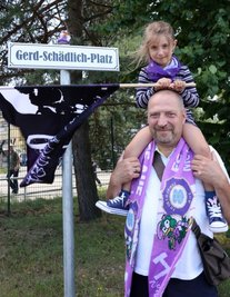 Direkt hinter dem Haupteingang zum Gelände des Erzgebirgsstadions zeigt dieses Schild: Hier ist jetzt der Gerd-Schädlich-Platz. Die aktive Fanszene hat die Namensänderung bereits vollzogen. Sie fordert jetzt die offizielle Umwidmung der Fläche. Im Bild FCE-Fan Dirk Natzschka aus Chemnitz mit seiner Tochter Serafina am Sonntag beim ersten Saison-Heimspiel gegen den VfL Osnabrück. 