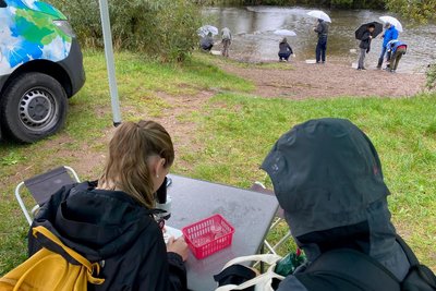 Petrissa und Nelly beobachten unter dem Mikroskop Fluss-Kleinlebewesen, während ihre Mitschüler Nachschub holen.