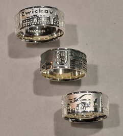 Auf silbernen Ringen sind Wahrzeichen und Wappen zu sehen.