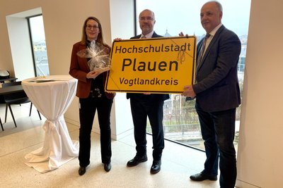 Professorin Katja Born, Oberbürgermeister Steffen Zenner (CDU) und Direktor Lutz Neumann mit dem Sinnbild für die Transformation in den Händen: einer kleinen Ausgabe des neuen Ortseingangsschildes.