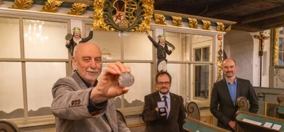 Münzfreunde-Vorsitzender Helmut Herholz (vorn) ließ es sich nicht nehmen, die ersten Exemplare persönlich in Scheibenberg vorbeizubringen. Er bedankte sich bei Pfarrer Stephan Schmidt-Brücken (Mitte) und Bürgermeister Michael Staib für die gute Zusammenarbeit. Im Hintergrund: die Bergmannsloge in der Kirche.