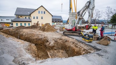 Die Baustelle aus Richtung des alten Rathauses in Johanngeorgenstadt gesehen: Der Graben diente dem Verlegen einer Strom- und einer Wasserleitung. Später entsteht hier der Anbau an das ehemalige Sparkassengebäude (hinten). Das neue Bürgerdienstleistungszentrum soll im November fertig sein, der Umzug der Verwaltung erfolgt 2023. 