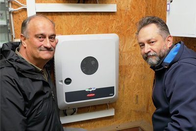 Christian Neubert (l.) und Thomas Welter an einem Hybrid-Wechselrichter. Damit werden die angeschlossenen Wechselstromverbraucher je nach Bedarf aus der solargespeisten Batteriebank oder der zweiten Stromquelle versorgt.