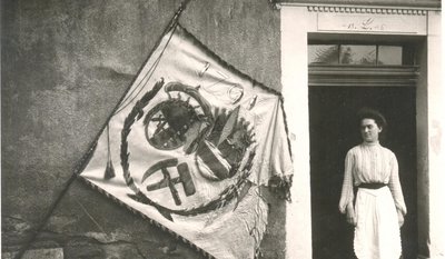 Die um 1920 entstandene Aufnahme zeigt die im Jahr 1791 historische Bergfahne vor dem Huthaus des Lampertus-Schachtes in Hohenstein-Ernstthal. Es ist nicht bekannt, wer die Frau auf dem Foto ist. 