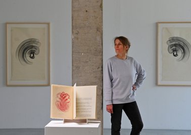 Galeristin Henriette Schneidewind neben einem Buch mit chinesischen Texten, das von der Leipziger KünstlerinMaribel Mas illustriert wurde. 