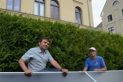 Alexander Spitzner von der TWV (links) mit Monteur Steffen Fröhlich an den Solarmodulen, die an der Böschung hinter der Stadtbibliothek Treuen angebracht sind. In den Modulen wird die Luft der Solarlüftung erwärmt, mit deren Hilfe der Keller des Bücher trockengelegt werden soll.