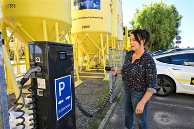 Sakret-Mitarbeiterin Angela Polster zeigt die neue Ladestation für E-Fahrzeuge wie Dienstautos und Baumaschinen, zum Beispiel Gabelstapler.