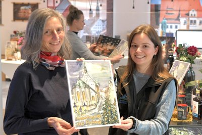 Ingunn Abraham (l.) zeigt Jasmin Faust von der Touristinformation am Schlossplatz in Freiberg den Silberstadt Freiberg Schoko-Adventskalender 2023, den sie gestaltet hat.