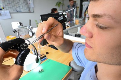 Jakob Füchtner zerlegt ein Uhrwerk mit einer Pinzette. Zum Schutz trägt der Uhrmacher Fingerlinge.
