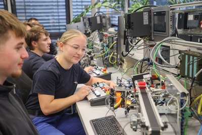 Sarah-Michelle Berger und die anderen Auszubildenden an einem Übungsmodell zum Programmieren von Industrieanlagen.