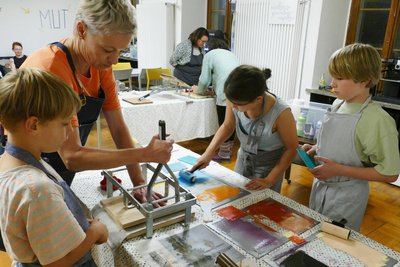 Hier ist Simone Illgen mit einigen Teilnehmern beim letzten Arbeitsschritt an der Druckpresse zu erleben.
