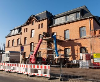 Mit einem Teleskopstapler wird Baumaterial in das erste Obergeschoss geschafft. Palettenweise stehen Putz und andere Baustoffe herum. Seit 2021 wird der Bahnhof in Mittweida umgebaut. Die Arbeiten dauern länger als gedacht und ziehen sich bis ins kommende Jahr hinein. 