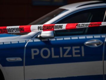             Ein Polizeiauto steht hinter einem Absperrband der Polizei.