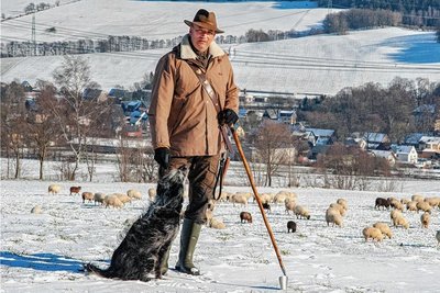 Wanderschäfer Jan Raupach mit einem seiner Hütehunde auf einer Weideflächen im Erzgebirge. Ohne den Filzhut geht er im Winter nicht auf Wanderung - der hält auch Regen stand. 