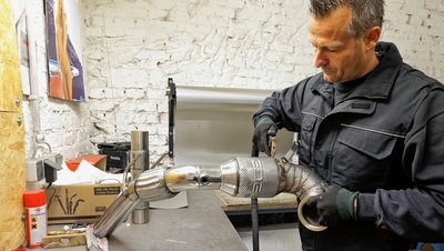 André Korb mit einer Downpipe, einer Verbindung zwischen Auspuff und Turbolader, für einen 7er Golf GTI. Das Firmenlogo ist gut sichtbar. Die Kunden sorgen mit Mund-zu-Mund-Propaganda für stetige Aufträge. 