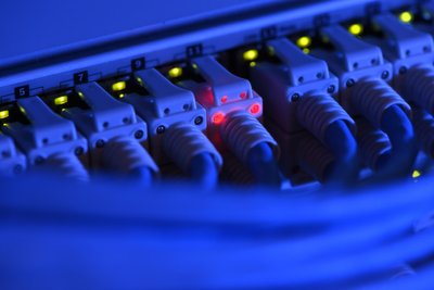 Ein Netzwerk-Kabelstecker leuchtet in der Netzwerkzentrale einer Firma zu Kontrollzwecken rot.