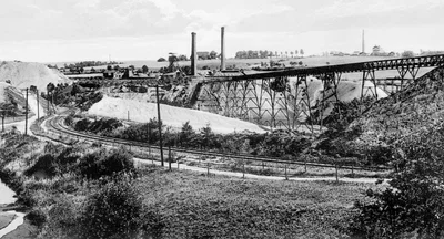 Im Vordergrund liegen die Gleise der Brückenbergkohlenbahn. 1921 wurde über das Pöhlauer Tal eine Stahlbrücke für die Hunteförderung zwischen den Brückenbergschächten I und II (im Bild) gebaut. Rechts hinten steht der Brückenbergschacht IV. 