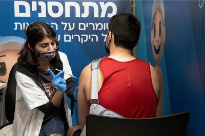In Israel sind die Booster-Impfungen gegen Corona in vollem Gang - auch für Jüngere. Eine medizinische Angestellte in Jerusalem verabreicht einem Mann eine dritte Dosis. 