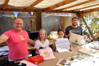 Elena (l. M.) und Greta lassen sich bei René Bach (l.) und Robert Zierold T-Shirts mit Buchholzer Motiven drucken. Foto: Robby Schubert