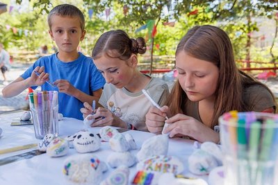 Sammy (8), Lucy (13) und Olivia (10) (v. l.), die regelmäßig in das Kulturzentrum kommen, bemalen Steine. Am Nebentisch steht eine Buttonmaschine.