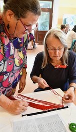 Marie-Pierrette Le Gac (links) erklärt Bettina Liebscher aus Olbernhau die Technik des Makramee. Sie ähnelt in gewisser Weise dem Klöppeln.