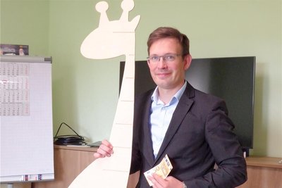 Bürgermeister Andreas Heinig zeigt die Begrüßungsgeschenke der Gemeinde für Neugeborene in Claußnitz. Eine Messlatte aus Holz fürs Kinderzimmer, die als Giraffe gestaltet ist, und 50 Euro.