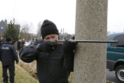 Ein Polizeibeamter zielt mit der Originalwaffe bei der Rekonstruktion der Tat auf den 70 Meter entfernten Streifenwagen.