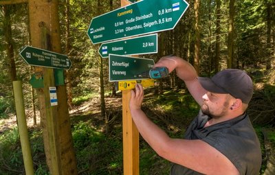 Peter Wießner, Vorarbeiter bei dem bauausführenden Unternehmen aus Lichtenberg, montiert an der Kreuzung von Hammerweg und A-Flügel die Beschilderung an einen neu gesetzten Pfahl - ein Bestandteil des 330 Kilometer langen Wanderwegenetzes, das die Stadt Olbernhau in Ordnung bringen lässt.