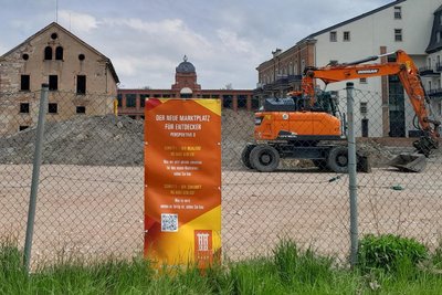 Der QR-Code auf den orangefarbenen Bannern am Bauzaun erlaubt via Smartphone einen grafisch animierten Blick auf den künftigen Marktplatz der Stadt Flöha.